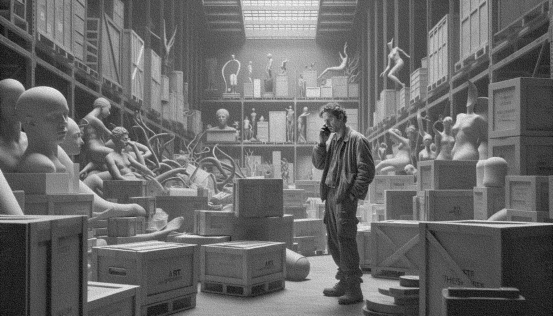 An art handler in overalls wrapping a scuplture of a chicken that is smoking a cigarette up in bubble wrap. The art handler looks like a hipster doofus with a man bun.